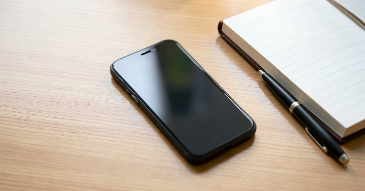 木のデスクの上に置かれたスマートフォンとノートの風景。